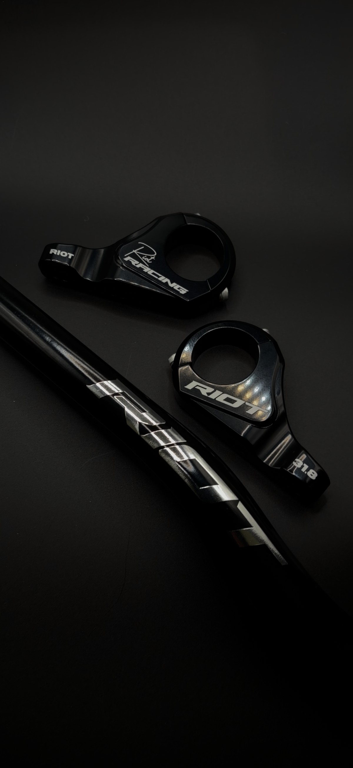 Black and chrome Riot Racing stem components beside a black handlebar.