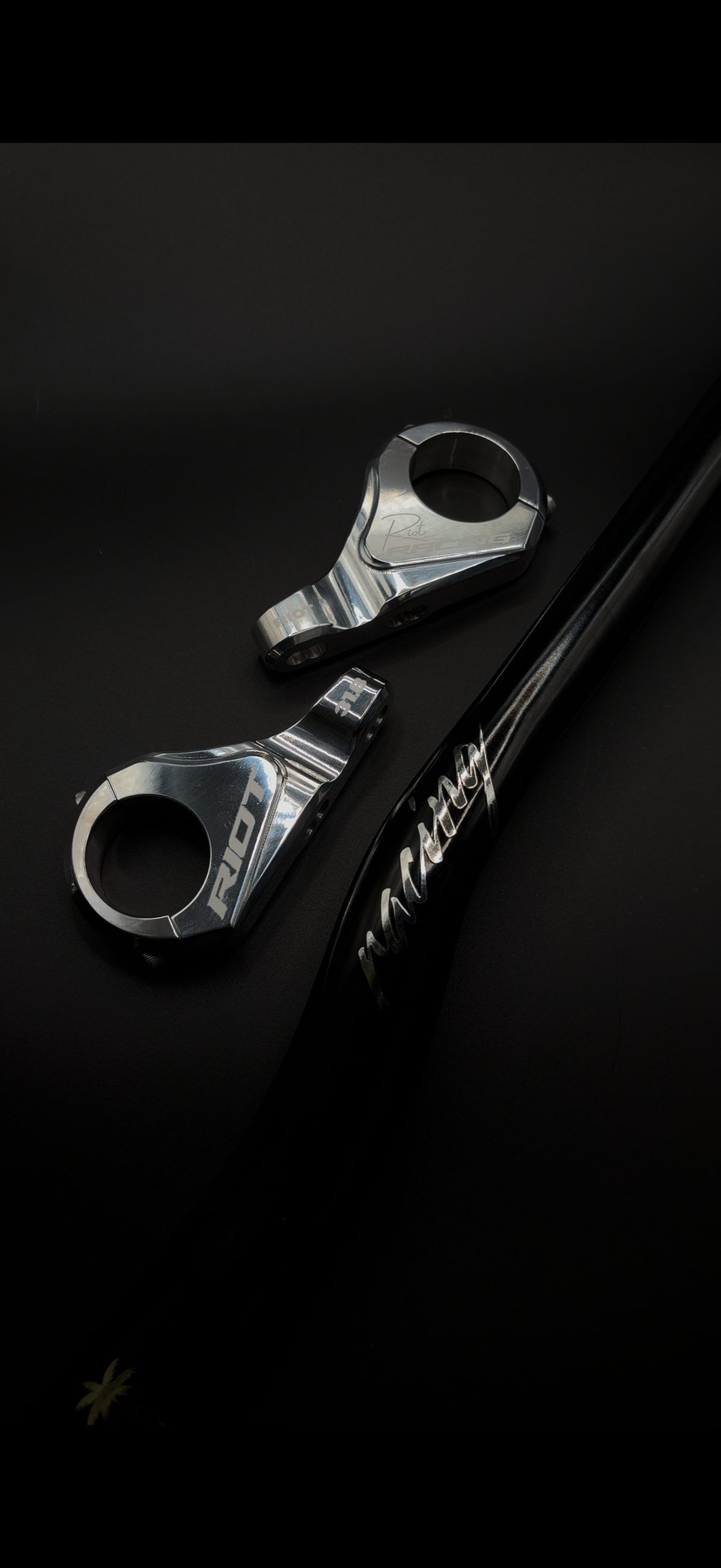 Two chrome Riot Racing stem components arranged beside a black handlebar on a dark background.