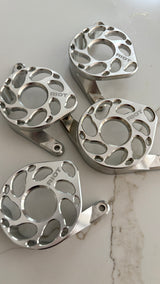Four polished Riot motor covers arranged on a light stone-patterned surface, showing their circular cutouts and mounting tabs.