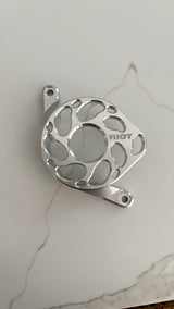 Overhead view of a polished Riot motor cover with a central opening and curved cutouts on a light stone-patterned surface.
