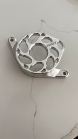 Angled view of a polished Riot motor cover, showing its raised rim and two mounting tabs on a light stone-patterned surface.
